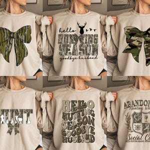 Op de afbeelding: Zes verschillende ontwerpen van beige sweatshirts met camouflage-printontwerpen. De ontwerpen omvatten een strik, de woorden "hello hunting season goodbye husband", het woord "hunt", de woorden "hello hunting season goodbye husband", een wapenschild met de woorden "abandoned hunting wives social club", en de woorden "hello hunting season goodbye husband".