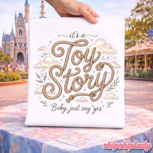 Puede incluir: Una camiseta blanca con un dise&ntilde;o gr&aacute;fico que presenta el texto "it's a Toy Story" escrito con una tipograf&iacute;a que imita una cuerda, rodeado de nubes y hojas ilustradas. Debajo del texto principal, la frase "Baby, just say "yes"" est&aacute; impresa.