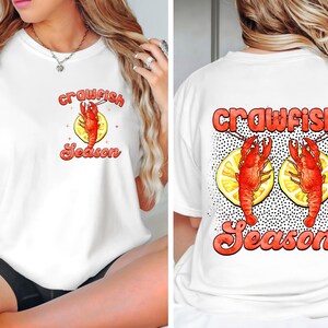 May include: White t-shirt with a red crawfish and lemon design. The text "crawfish season" is printed in red on the front and back of the shirt.