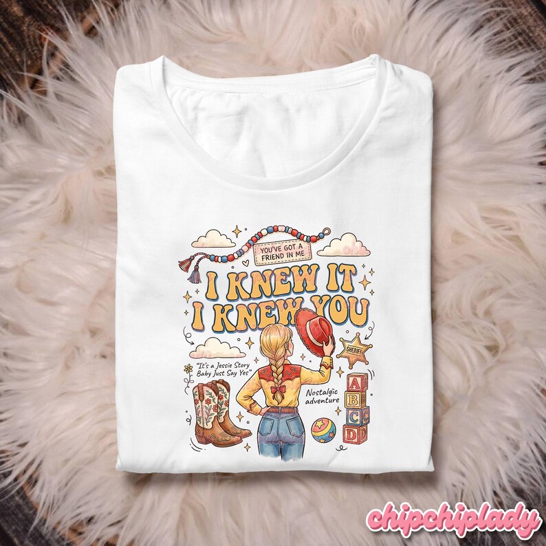 May include: A white t-shirt featuring a graphic illustration of a person with a blonde braid wearing a yellow shirt and blue jeans. The design includes cowboy boots, a red hat, alphabet blocks, and the text "I KNEW IT I KNEW YOU" and "YOU'VE GOT A FRIEND IN ME".