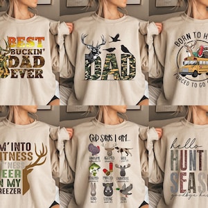 Op de afbeelding: Set van tien beige sweatshirts met verschillende jacht-thema ontwerpen. De ontwerpen omvatten herten, een schoolbus en tekst zoals "Best Buckin' Dad Ever", "Born to Hunt", "I'm into Fitness Deer in My Freezer", en "God Says I Am..."