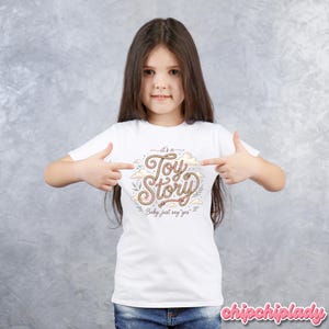 Puede incluir: Una camiseta blanca de manga corta con un dise&ntilde;o gr&aacute;fico que presenta el texto "it's a Toy Story" escrito en una fuente estilo cuerda, rodeado de ilustraciones de nubes y hojas peque&ntilde;as, con el texto adicional "Baby, just say yes" debajo.