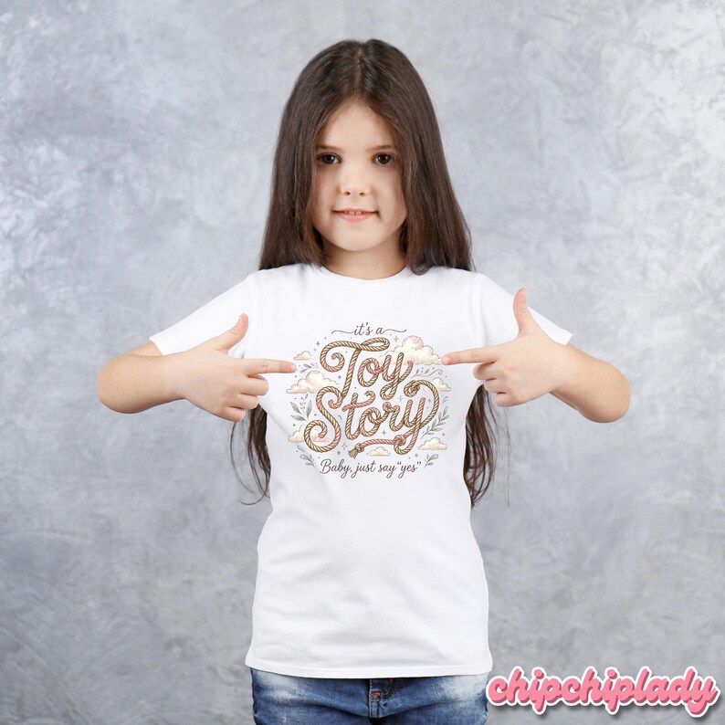 Puede incluir: Una camiseta blanca de manga corta con un dise&ntilde;o gr&aacute;fico que presenta el texto "it's a Toy Story" escrito en una fuente estilo cuerda, rodeado de ilustraciones de nubes y hojas peque&ntilde;as, con el texto adicional "Baby, just say yes" debajo.