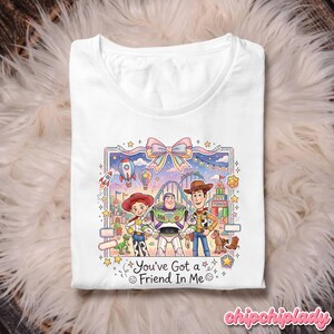 Peut inclure: T-shirt blanc avec un graphisme color&eacute; des personnages de Toy Story. Le design comprend Woody, Buzz l'&Eacute;clair et Jessie, avec le texte "You've Got a Friend In Me".