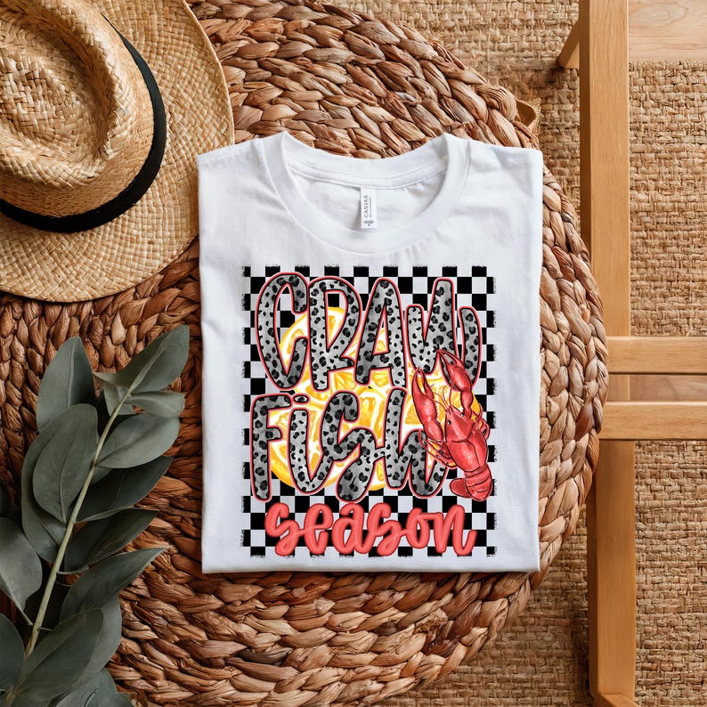 May include: White t-shirt with a black and white checkered background. The text "Crawfish Season" is written in red and black letters with a crawfish illustration in the center.