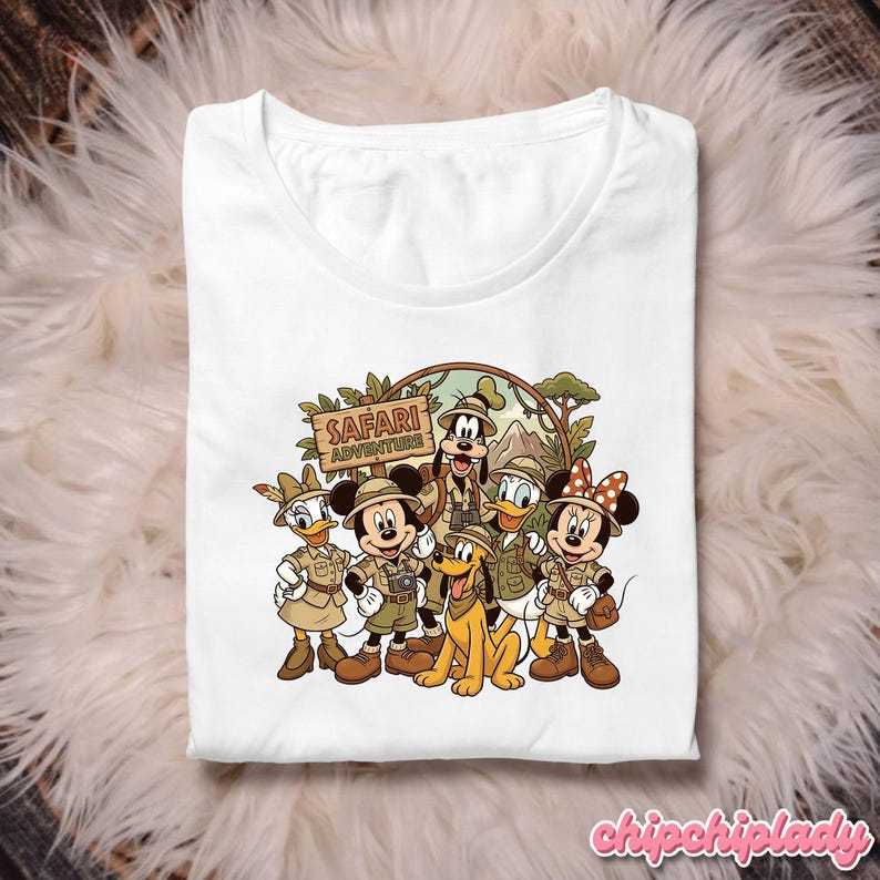 Puede incluir: Camiseta blanca con un gr&aacute;fico colorido de personajes de Disney vestidos con atuendos de safari. El dise&ntilde;o incluye a Mickey Mouse, Minnie Mouse, Donald Duck, Daisy Duck, Goofy y Pluto, con las palabras "Safari Adventure" en un letrero.