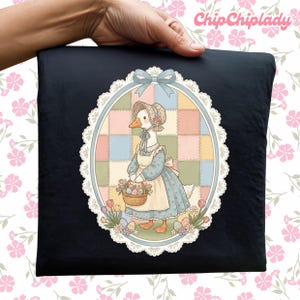 May include: Black pillow with a whimsical illustration of a goose wearing a bonnet and apron, carrying a basket of eggs and flowers. The artwork is framed by a white lace-like border and a blue bow. The text "ChipChipLady" is in the upper right corner.