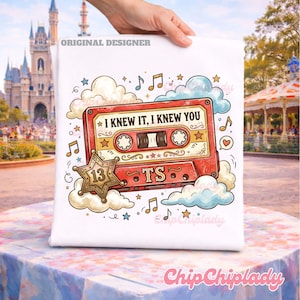 May include: A white t-shirt featuring a graphic of a red cassette tape with the text I KNEW IT, I KNEW YOU. The design includes a gold star with the number 13, the letters TS, musical notes, hearts, and light blue and cream-colored clouds.