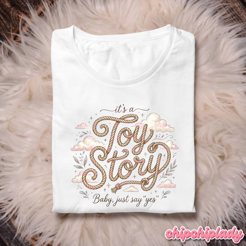 Puede incluir: Una camiseta blanca con un dise&ntilde;o gr&aacute;fico que presenta el texto "it's a Toy Story" escrito en una fuente que imita una cuerda. El dise&ntilde;o incluye ilustraciones de nubes rosas suaves, peque&ntilde;as estrellas y delicadas hojas verdes, con el texto "Baby, just say "yes"" debajo.