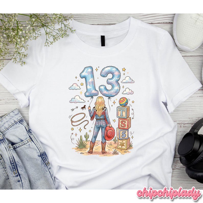 Pu&ograve; includere: Una t-shirt bianca con la grafica di una persona dai capelli biondi che indossa un cappello da cowboy, jeans e stivali. Il design include il numero 13 in stile palloncino, un lazo, una pila di blocchi con le lettere T, S, S e una palla.