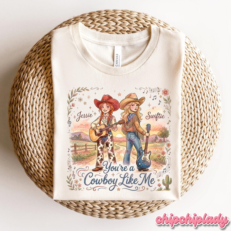 Pu&ograve; includere: Una t-shirt color crema con una grafica di due cowgirl in un paesaggio con il testo Jessie, Swiftie e You're a Cowboy Like Me. L'illustrazione include note musicali, fiori, un cactus e chitarre in una delicata tavolozza di colori.