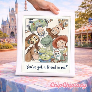 May include: White square pillow featuring a watercolor illustration of Toy Story characters, including Woody, Buzz Lightyear, and Jessie. The text "You've got a friend in me" is written below the image. The pillow is held by a hand.