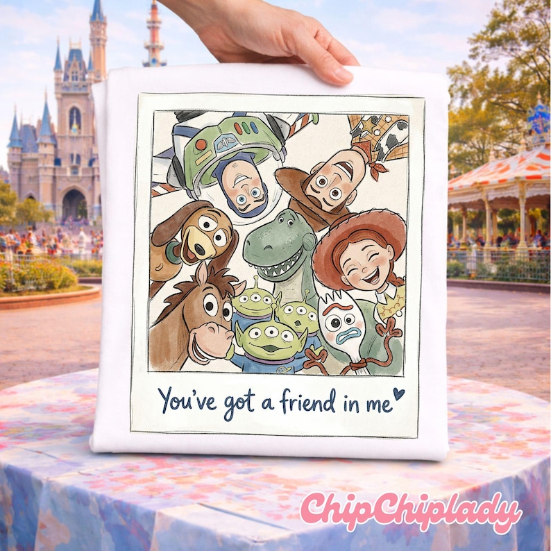 May include: White square pillow featuring a watercolor illustration of Toy Story characters, including Woody, Buzz Lightyear, and Jessie. The text "You've got a friend in me" is written below the image. The pillow is held by a hand.