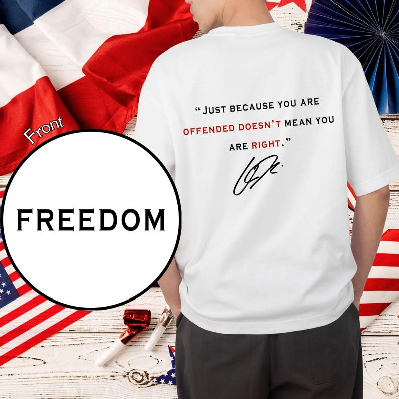 Peut inclure: T-shirt blanc avec le texte "JUST BECAUSE YOU ARE OFFENDED DOESN'T MEAN YOU ARE RIGHT." en noir et rouge. Le mot "FREEDOM" est imprim&eacute; sur un cercle blanc. Le t-shirt est entour&eacute; de drapeaux am&eacute;ricains et fran&ccedil;ais.