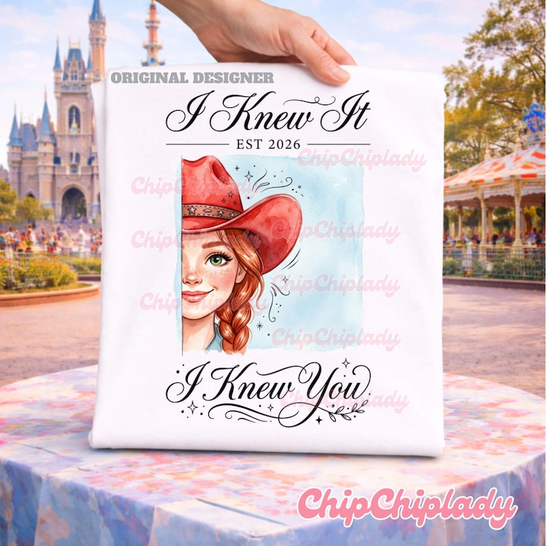 May include: A white t-shirt featuring a graphic illustration of a person with red hair wearing a red cowboy hat. The text reads "I Knew It", "EST 2026", and "I Knew You" in black cursive and serif fonts, set against a light blue watercolor background.