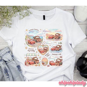 May include: White t-shirt featuring a colorful graphic of cartoon cars in various summer scenes. The design includes text that reads "summer besties", "forever my buddy", "bestie vibes", and "summer ride". The shirt has a crew neck and short sleeves.