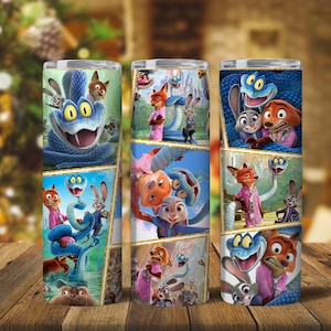 May include: Three tall, cylindrical tumblers with colourful cartoon character designs. Each tumbler features a collage of images with a blue snake, a fox in a pink shirt, and a rabbit. The tumblers are on a wooden surface.