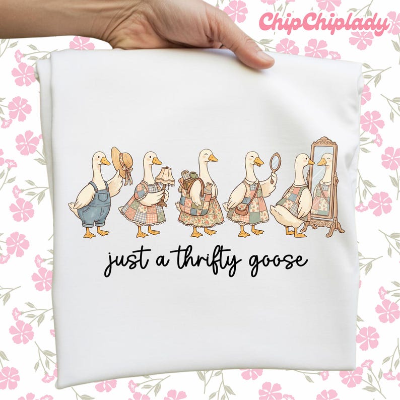 May include: White t-shirt featuring a whimsical illustration of six geese dressed in various outfits, including overalls, dresses, and accessories. The text "just a thrifty goose" is printed below the geese.