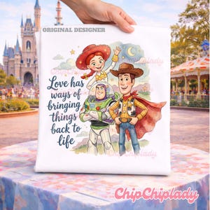 May include: A white t-shirt featuring a colorful illustration of Jessie, Buzz Lightyear, and Woody from Toy Story. The text reads, Love has ways of bringing things back to life. The design includes a crescent moon, stars, and clouds in a watercolor style.