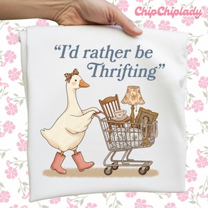 May include: White t-shirt featuring a cartoon goose wearing a bow and pink boots, pushing a shopping cart filled with vintage items. The text reads, "I'd rather be Thrifting."