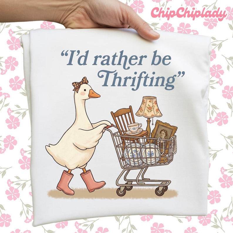 May include: White t-shirt featuring a cartoon goose wearing a bow and pink boots, pushing a shopping cart filled with vintage items. The text reads, "I'd rather be Thrifting."