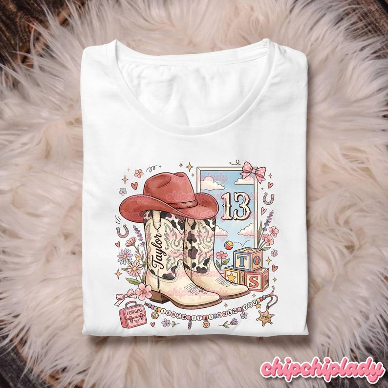 Pode incluir: Uma t-shirt branca com uma ilustra&ccedil;&atilde;o gr&aacute;fica de um chap&eacute;u de cowboy rosa sobre um par de botas western com padr&atilde;o de vaca. O design inclui o nome Taylor, o n&uacute;mero 13, blocos de alfabeto, flores e o texto I KNEW IT I KNEW YOU.