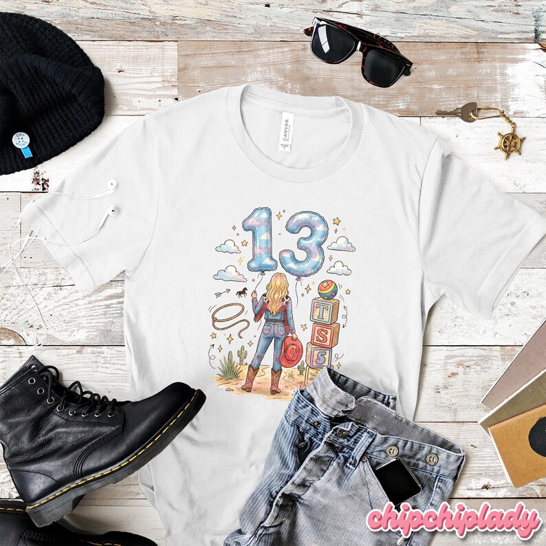 Pu&ograve; includere: Una t-shirt bianca a maniche corte con un'illustrazione grafica di una persona in abbigliamento western che tiene un lazo, vicino a blocchi impilati con le lettere T, S, S e due grandi palloncini blu che formano il numero 13 con motivi a nuvole.