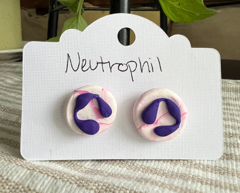 May include: A pair of purple and pink swirl polymer clay earrings with the word "Neutrophil" written on a white card.