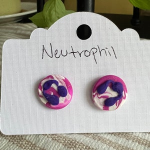 May include: A pair of purple and white swirl stud earrings with a purple neutrophil design. The earrings are on a white card with the word "Neutrophil" written on it.