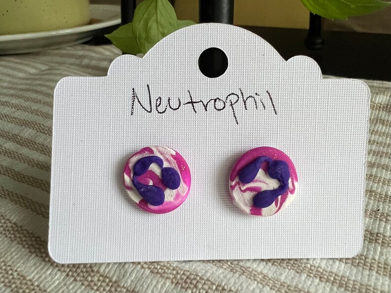 May include: A pair of purple and white swirl stud earrings with a purple neutrophil design. The earrings are on a white card with the word "Neutrophil" written on it.