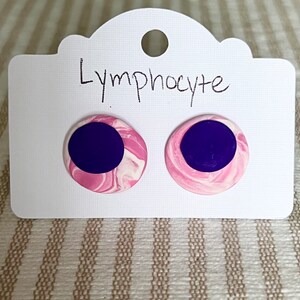 May include: A pair of pink and purple earrings with a marbled design. The earrings are labeled "Lymphocyte".