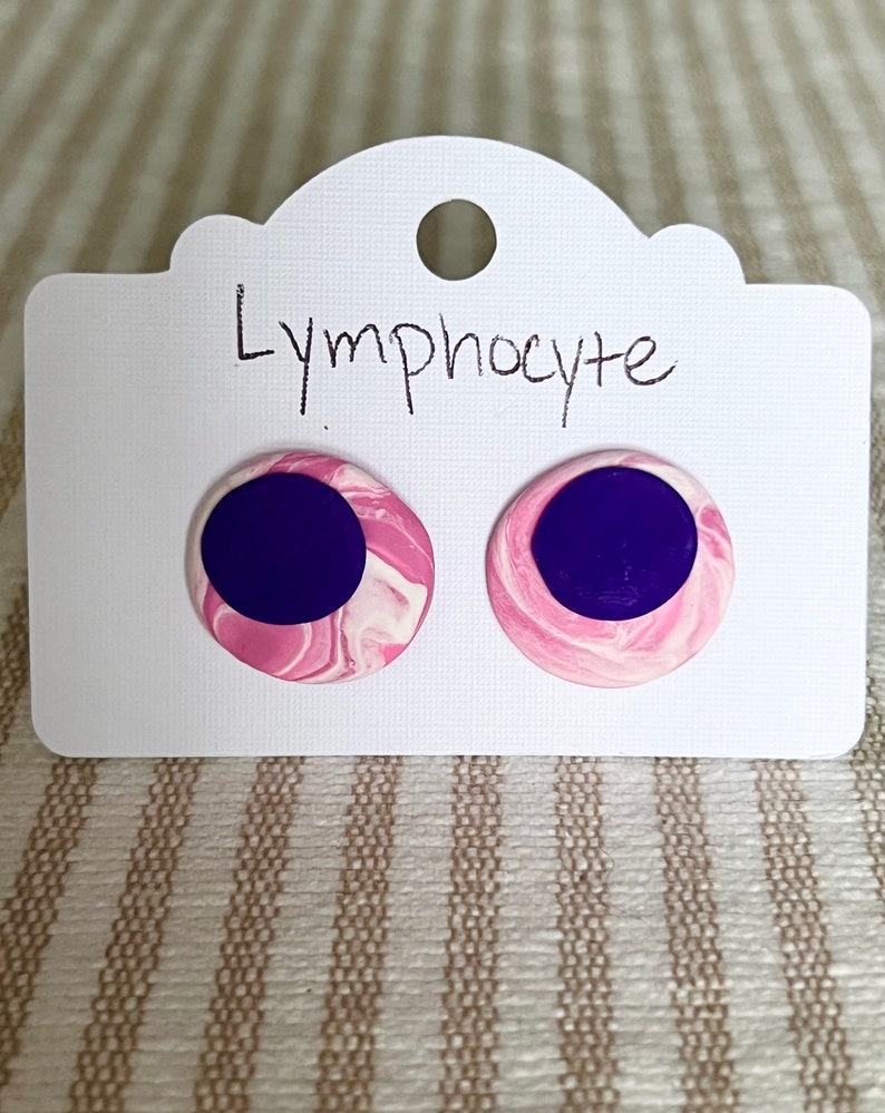 May include: A pair of pink and purple earrings with a marbled design. The earrings are labeled "Lymphocyte".