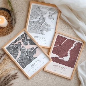 May include: Three framed city map prints. Two maps are of Boston, Massachusetts, and one is of Montreal, Quebec. The Boston maps are in black and white and black and pink. The Montreal map is in burgundy. All are in light wood frames.