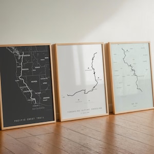 May include: Three framed map prints against a wall. The maps are in monochrome, with the Pacific Crest Trail labeled on one. The frames are light wood, and the maps are on a white background.