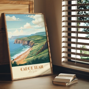 May include: A framed poster with a vintage travel illustration of a coastal landscape. The poster features a scenic view of a rocky coastline with a sandy beach and turquoise water. The text "CABOT TRAIL Nova Scotia" is printed at the bottom of the poster.