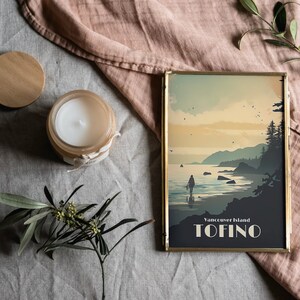 May include: A gold-framed print with a vintage-style illustration of a person walking on a beach with mountains and trees in the background. The text "Vancouver Island TOFINO" is printed at the bottom of the print.