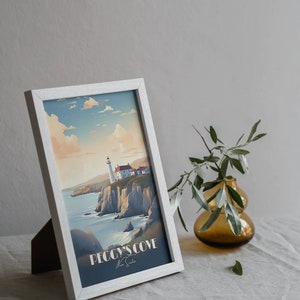 K&ouml;nnte beinhalten: Ein wei&szlig; gerahmter Druck eines Leuchtturms auf einer Klippe mit Blick auf das Meer. Der Druck tr&auml;gt den Titel "Peggy's Cove" mit der Unterschrift des K&uuml;nstlers darunter. Der Druck liegt auf einer wei&szlig;en Leinentischdecke mit einer kleinen Vase mit Gr&uuml;nzeug rechts.