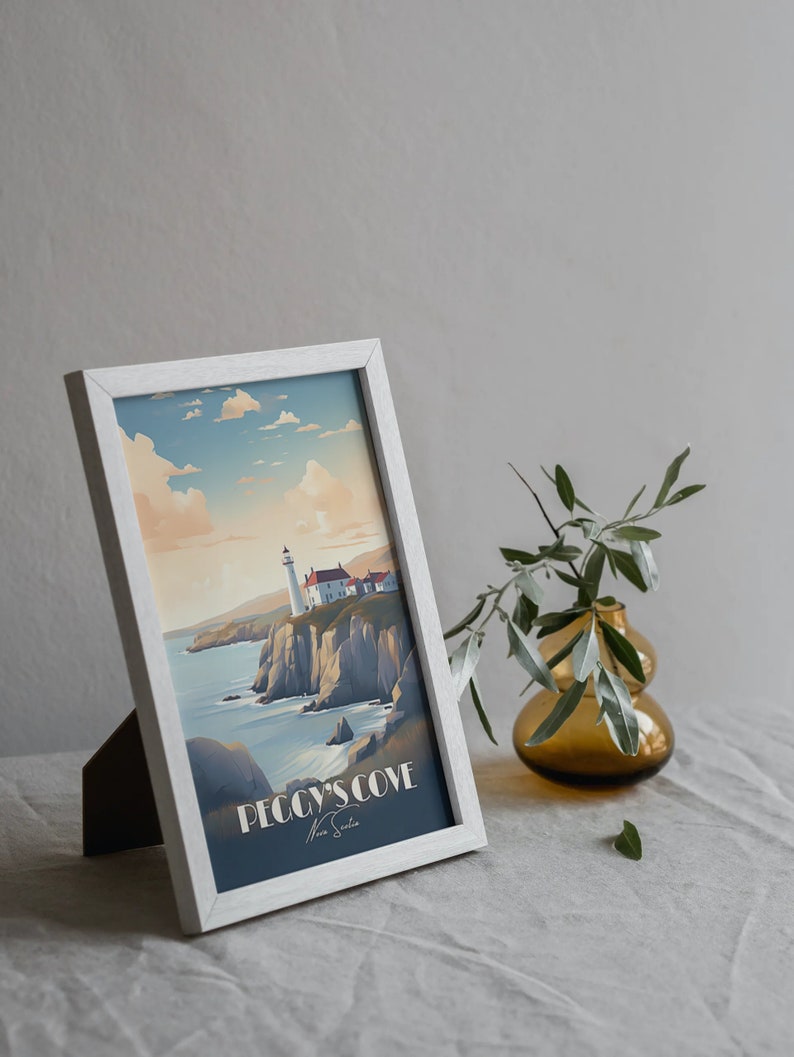K&ouml;nnte beinhalten: Ein wei&szlig; gerahmter Druck eines Leuchtturms auf einer Klippe mit Blick auf das Meer. Der Druck tr&auml;gt den Titel "Peggy's Cove" mit der Unterschrift des K&uuml;nstlers darunter. Der Druck liegt auf einer wei&szlig;en Leinentischdecke mit einer kleinen Vase mit Gr&uuml;nzeug rechts.