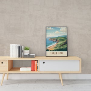 May include: A framed vintage travel poster depicting a scenic view of the Cabot Trail in Nova Scotia, Canada. The poster features a coastal landscape with a winding road, green hills, and a blue ocean. The text on the poster reads "Cabot Trail Nova Scotia".