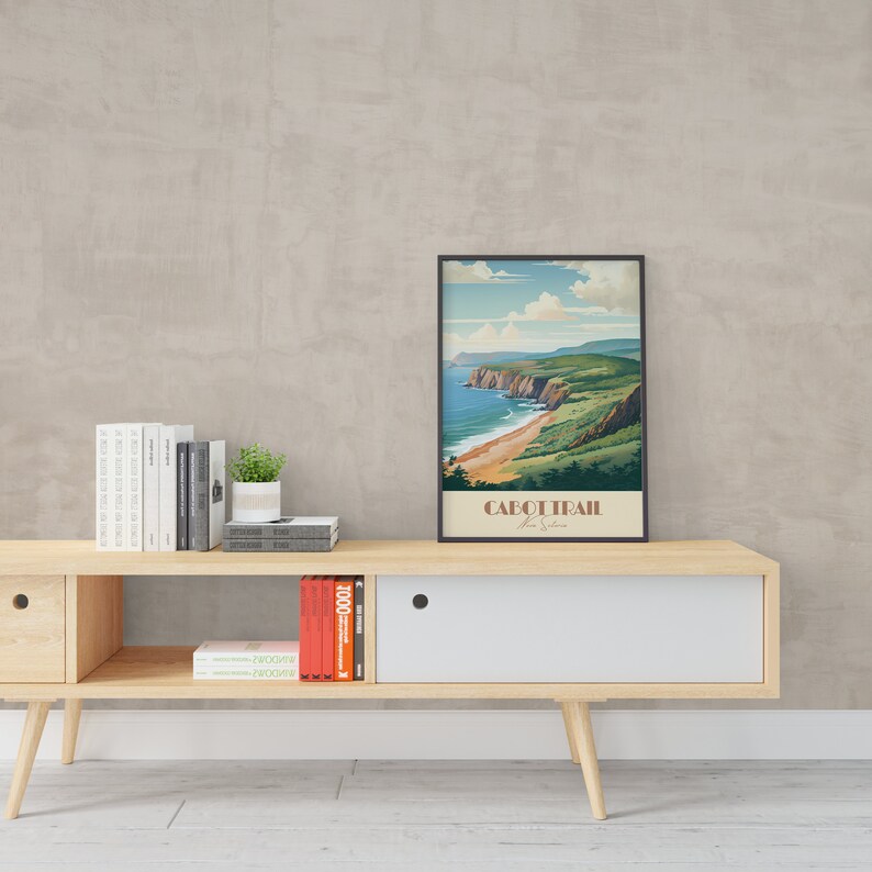 May include: A framed vintage travel poster depicting a scenic view of the Cabot Trail in Nova Scotia, Canada. The poster features a coastal landscape with a winding road, green hills, and a blue ocean. The text on the poster reads "Cabot Trail Nova Scotia".