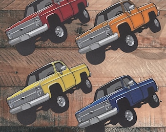 Può includere: Quattro pick-up vintage di diversi colori: rosso, arancione, giallo e blu. I pick-up sono tutti rivolti in avanti e hanno un design simile. Sono tutti su uno sfondo di legno.