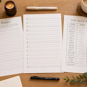 May include: Three white educational worksheets with black text and lines for handwriting practice. The sheets are titled The Basics and TOP SIGHT WORDS, featuring rows of letters and words to trace and copy, arranged on a wooden surface with pens.
