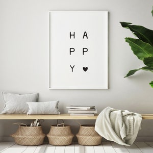 Könnte beinhalten: Ein weißer gerahmter Druck mit dem Wort "HAPPY" in schwarzen Buchstaben geschrieben, neben dem "Y" ein kleines schwarzes Herz. Der Druck hängt an einer weißen Wand über einer Holzbank mit einer weißen Wolldecke, zwei weißen Kissen und drei geflochtenen Körben.
