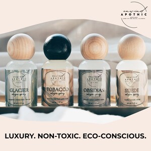 以下が含まれることがあります： 木製と黒色の球形トップが付いた、4つの薬局スタイルのコロン スプレーボトル。 各ボトルには、Glacier、Tobacco、Obsidian、Suedeという異なる香りの名前がラベルに記載されています。 テキスト「LUXURY. NON-TOXIC. ECO-CONSCIOUS.」が一番下にあります。