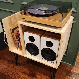 May include: A wooden record player stand with a turntable and two white speakers. The stand has black hairpin legs and a shelf for storing records.
