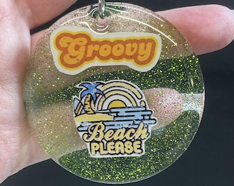 May include: A round, clear, green glitter keychain with a yellow, orange, and blue beach scene and the text "Groovy" and "Beach Please".