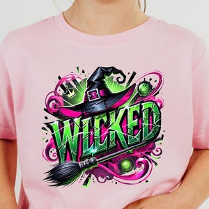 May include: Pink t-shirt with a colorful "WICKED" graphic. The design features a witch hat, broom, and the word "WICKED" in green and black. The shirt is worn by a child.