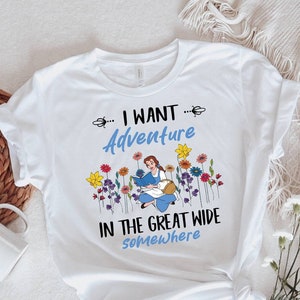 May include: White t-shirt with a graphic of a woman sitting in a field of flowers. The text on the shirt reads "... I WANT ... Adventure in the great wide somewhere."