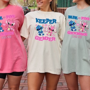 May include: Three short-sleeved t-shirts in pink, cream, and green. Each shirt features a cartoon character design with text. The pink shirt says "BLUE or PINK SARAH loves you." The cream shirt says "KEEPER of the GENDER." The green shirt says "BLUE or PINK GRANDMA loves you."