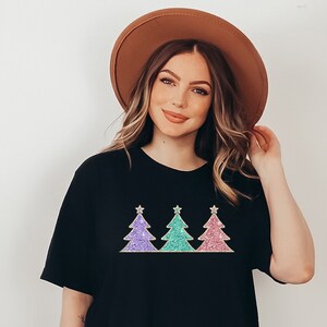 May include: A black t-shirt with a design of three glitter Christmas trees in pink, green, and purple.